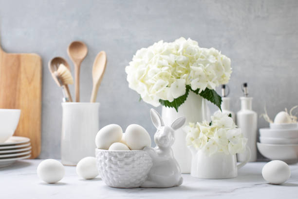 Easter decorations such as  porcelain bunny and eggs on a kitchen countertop decorated with fresh flowers, front view