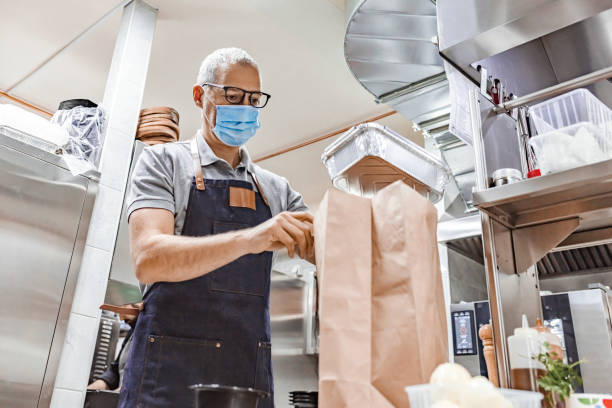 istock Masked Restaurant Employee Bagging Up To-Go Order During Covid-19 Lockdown 1305053552