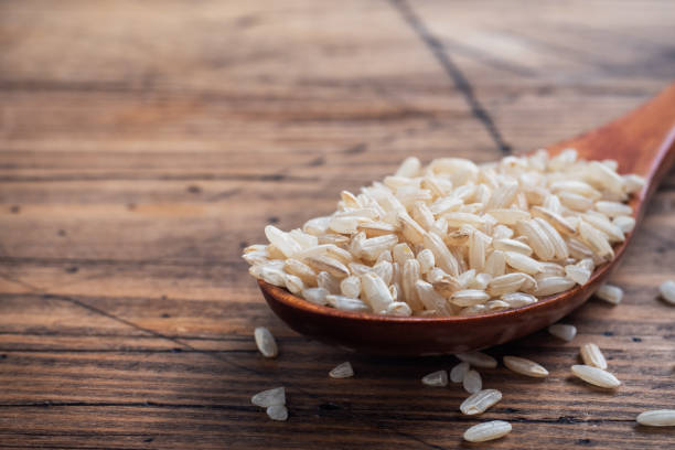 istock Brown rice raw long grain in a spoone, wooden background copy space. 1305059511