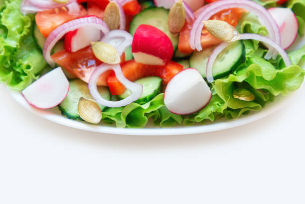 Close-up of a fresh salad of cucumbers, tomatoes, radishes, onions and other vegetables on a plate for a healthy meal. Isolated on a white background. Copy space. Selective focus