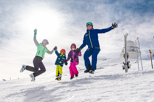 Adult on skiing slope glide backwards teaching little child to ski going downhill holding poles in hands
