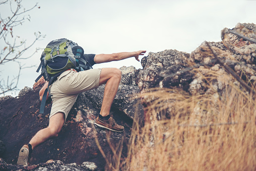 Hiker man climbing natural rocky wall with tropical valley on the background.   people backpack walking trail activity camping outdoors for destination leisure.  People happy feeling freedom good and strong  victorious facing on the natural mountain