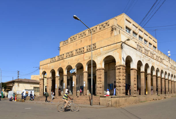Asmara, Eritrea: people outside a colonial commercial building with shady colonnade aligned with Seraye Street - Eritrea Square / Piazza Italia, originally larger and called Piazza del Grande Mercato - on the right Barentu Street and on the left  Dekemhare Street - Asmera, a Modernist City of Africa - UNESCO World Heritage Site.