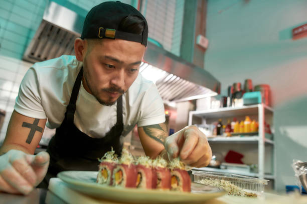 Portrait of experienced sushi chef carefully adding final touch with dedication to his delicious sushi set Portrait of experienced sushi chef carefully adding final touch with dedication to his delicious sushi set. Japanese cuisine, restaurant service, business concept cooking show stock pictures, royalty-free photos & images
