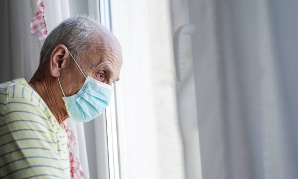 istock Gray haired senior man wearing medical face mask looking through window. 1305076255
