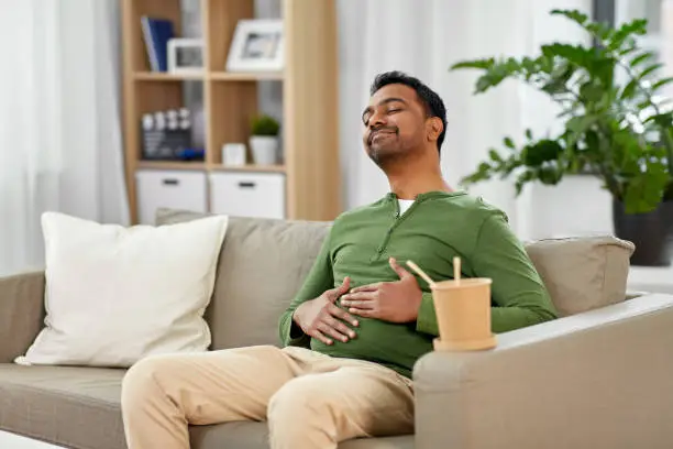 Photo of pleased indian man eating takeaway food at home