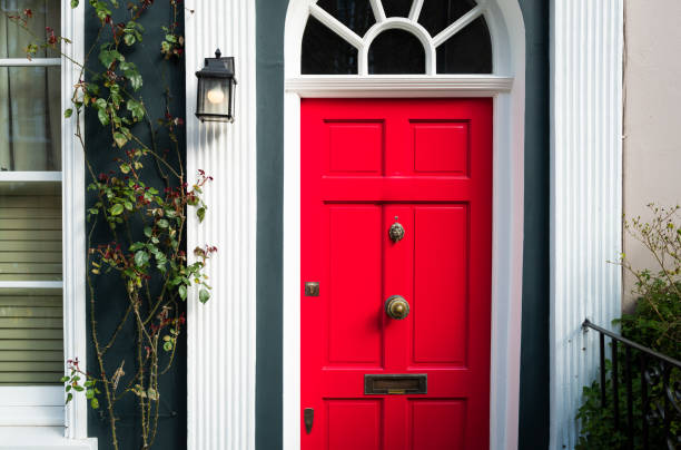 Color image depicting the exterior of a building on a traditional city street in Hampstead, an affluent area of London, UK. The house has a pretty red door, red brick walls, and the facade is decorated with a lush, verdant green bush. Room for copy space.