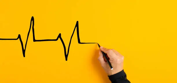 Photo of Male hand drawing a electrocardiogram heart beat chart on yellow background. Heart health care and medical check up