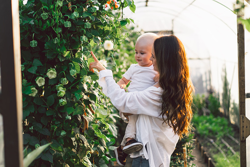 Woman playing with her child in a greenhouse with flowers. Happy Mother's Day