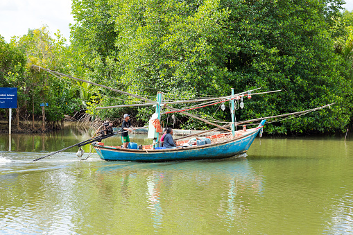 Small Thai fisher boat with men on river in Chumphon province near coast.  men are passing rainforest on way to coast and sea. River is Phanng Tak.
