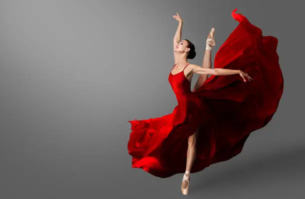 Ballerina Dance. Ballet Dancer in Red Dress jumping Spit. Woman in Ballerina Shoes dancing in Evening Silk Gown flying on Wind in Air. Black background with Copy Space