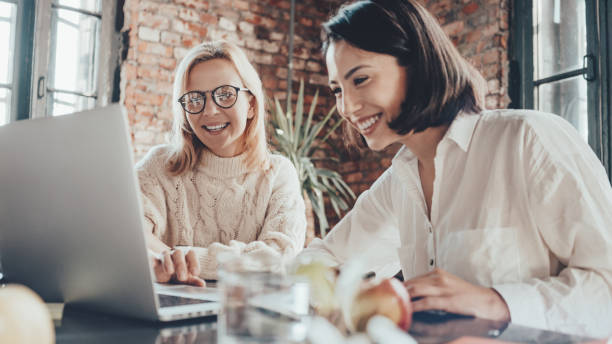 Two handsome business woman working together with laptop and sitting at the desk stock photo