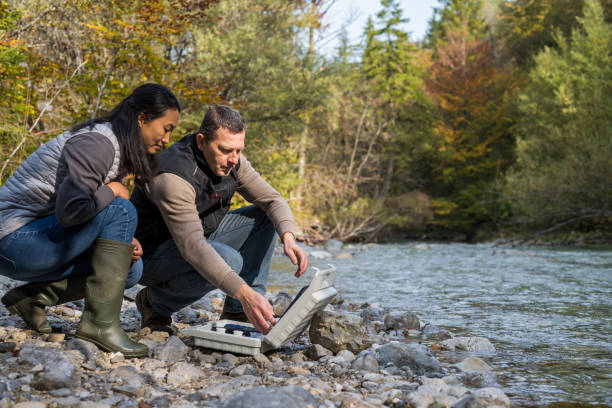 istock Man and woman squatting at case with testing equipment. Analyzing water quality in mountain river. 1305091880