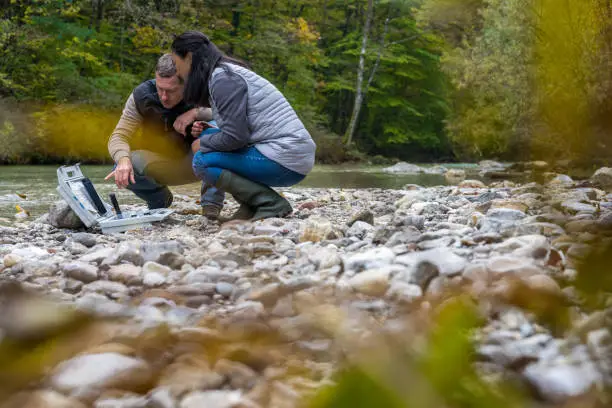Two colleagues analyzing water quality in mountain river. Biological researchers at fieldwork. Environmental protection, biological research concept.