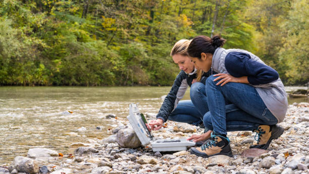 istock Female colleagues discussing data in digital tablet. Two women squatting at riverside. 1305091941