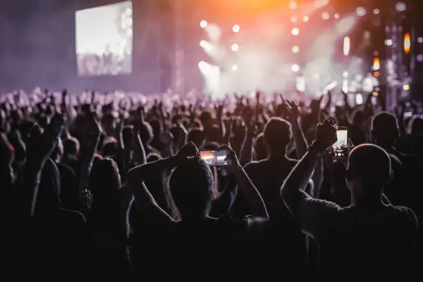 Photo of People with raised hands, silhouettes of concert crowd in front of bright stage lights.