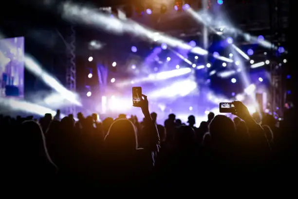 Photo of People with raised hands, silhouettes of concert crowd in front of bright stage lights.