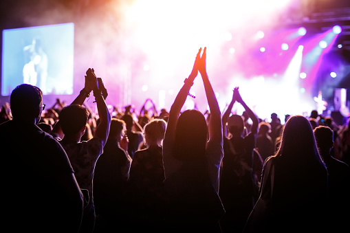 Personas con las manos levantadas, siluetas de público de conciertos frente a luces brillantes del escenario. photo