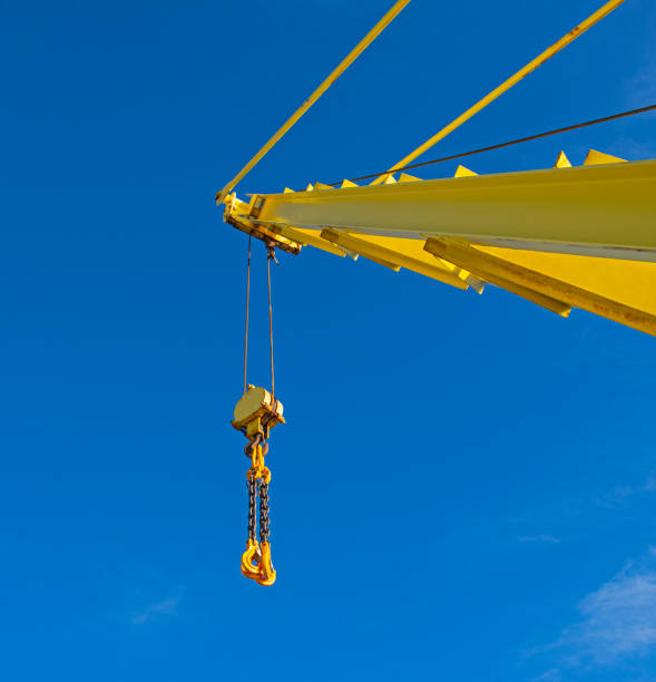 Large crane jib against blue sky background Large extended industrial crane jib boom arm against a blue sky background with block tackle jib stock pictures, royalty-free photos & images