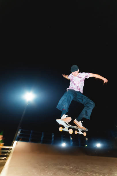 istock Young guy skateboarder doing a jump trick at night in a skatepark 1305099645