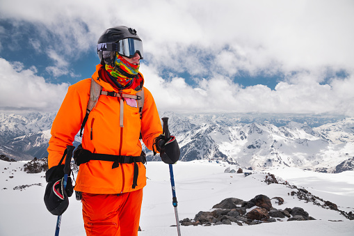 Young sportsman skier in mask with ski stick on the background of the Caucasian mountains.