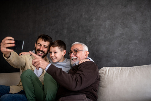 Father is taking selfies with a young boy and senior adult. They are happy to share moments, enjoying Father's day. Copy-space.