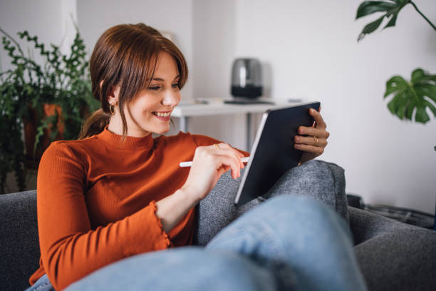 ビジネスの女性:自宅でデジタルタブレットを使用して笑顔の若いビジネスウーマン - digital tablet businesswoman young women watching ストックフォトと画像