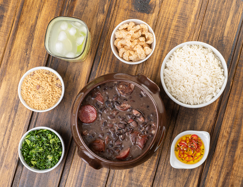 Traditional brazilian feijoada with kale, manioc flour, rice, pepper, cracklings and caipirinha.