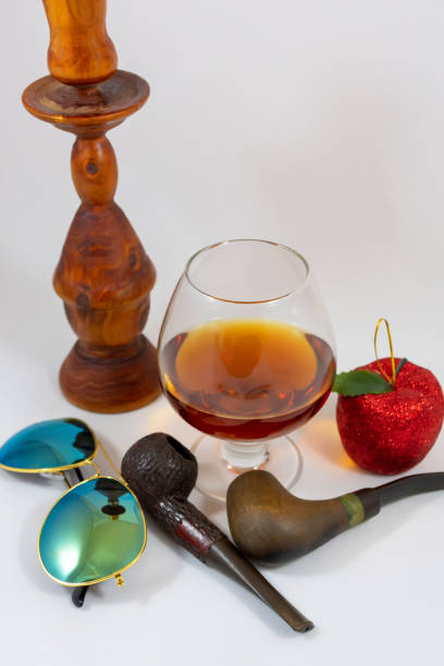 Tobacco carved dark brown smoking pipe and whiskey in the tall glass on the wooden table.
