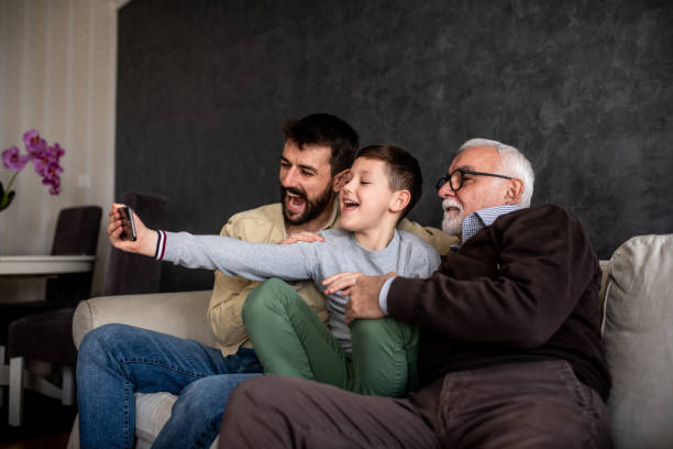 Little boy is taking selfie with his daddy and granddaddy. The smiling boy is taking a selfie with his father and grandfather. They are sitting in the living room on the sofa bed. Father's day concept. father son grandfather fathers day stock pictures, royalty-free photos & images