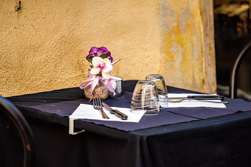 Closeup of two glasses on empty restaurant table in Italy, Italian cafe outside with orange yellow wall and blue purple tablecloth color with flowers
