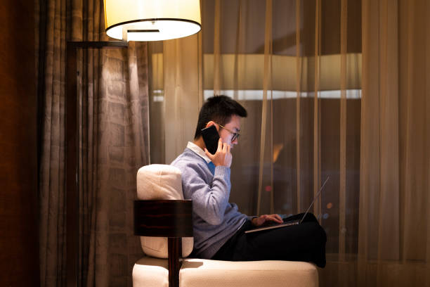 istock Asian man making a call while working at home with laptop at night by the window 1305108786