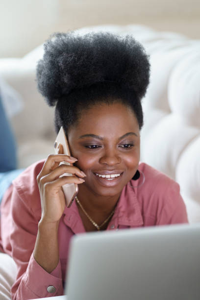istock Smiling Woman Talking Over Mobile Phone While Using Laptop 1305112162