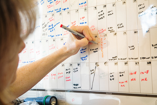 Mature confident left handed female writing down success on her wall calendar on the date her goals will be met.