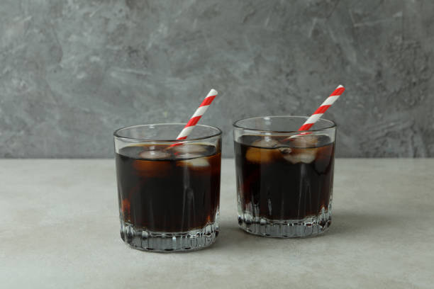 istock Glasses of cola on white textured table against gray background 1305117016
