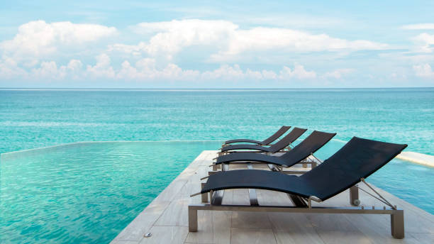 istock Luxury poolside with sun beds and deck chairs over blue sea. Tranquil luxury vacation background. Recreational and relaxing beach scene 1305118365