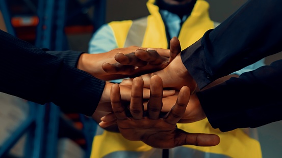 Factory workers stacking hands together in warehouse or storehouse . Logistics , supply chain and warehouse business concept .