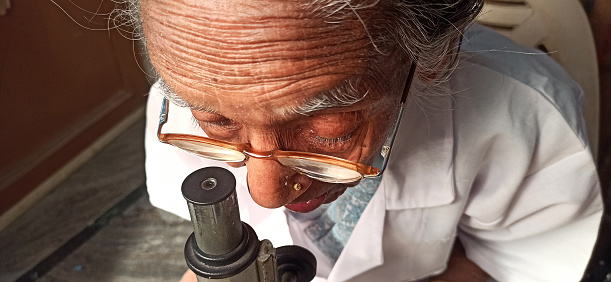 an old woman is searching for a new cell under the microscope ,