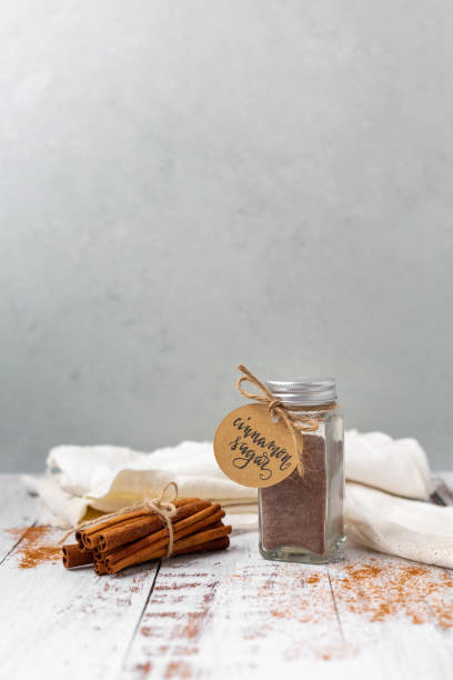 istock Jar of Cinnamon Sugar on a White Table with Gray Background; Bundle of Cinnamon Sticks and Ground Cinnamon on Table 1305130940