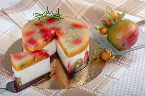 Refreshing cake with gelatin and fruit. The cake is filled with cream cheese and mango puree and decorated with rosemary. In the bowl next to the cake is mango and cape gooseberry.