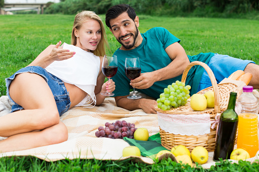 Man and woman are lying and relaxing with wineglasses on picnic outdoor.