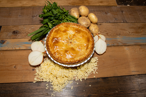 A delicious meat pie top down view showing the tasty meat pie and crust topping on a wooden kitchen table surrounded by the ingredients used to make the golden pie