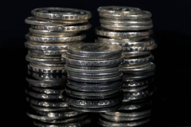 Close-up of a quarter on top of a stack of coins, with USD bills in the background.