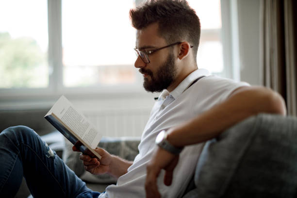 istock Young man reading a book at home 1305141912