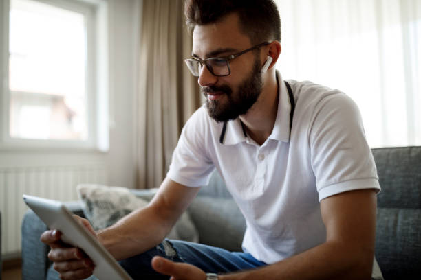 istock Smiling young man with bluetooth headphones using digital tablet at home 1305141930