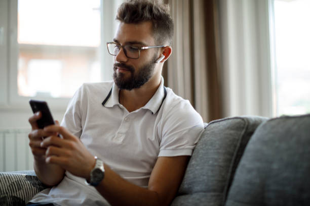 istock Young man with wireless headphones using mobile phone at home 1305142091