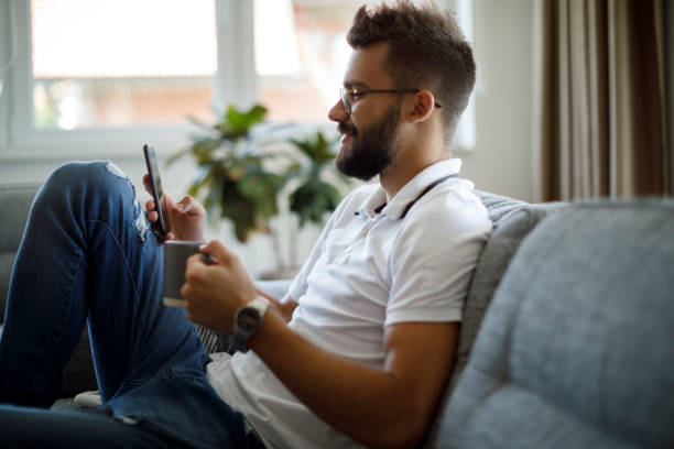 istock Smiling young man drinking coffee and texting on the phone at home 1305142143
