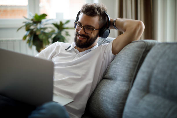 istock Young smiling man with bluetooth headphones using laptop at home 1305142307