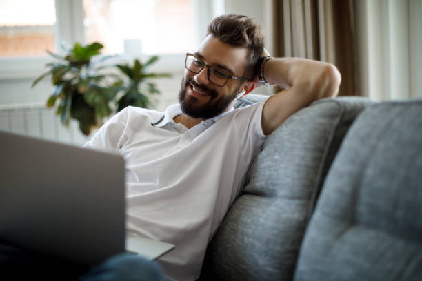 istock Young smiling man with bluetooth headphones using laptop at home 1305142949