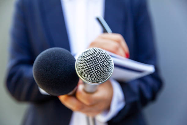 Female journalist at news conference or media event, writing notes, holding microphone stock photo
